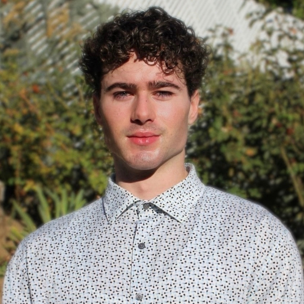 Man in a light colored patterned button up with short dark curly hair