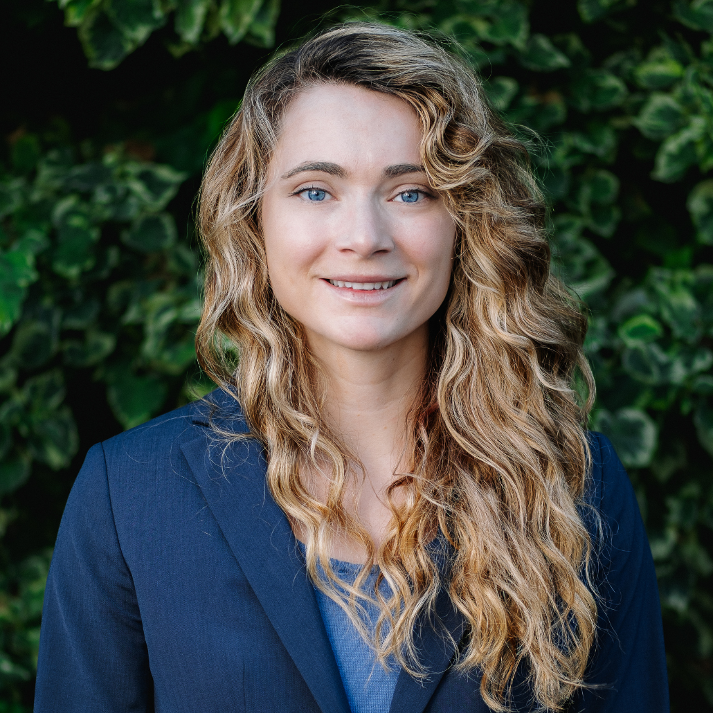 A woman in a blazer standing in front of foliage 