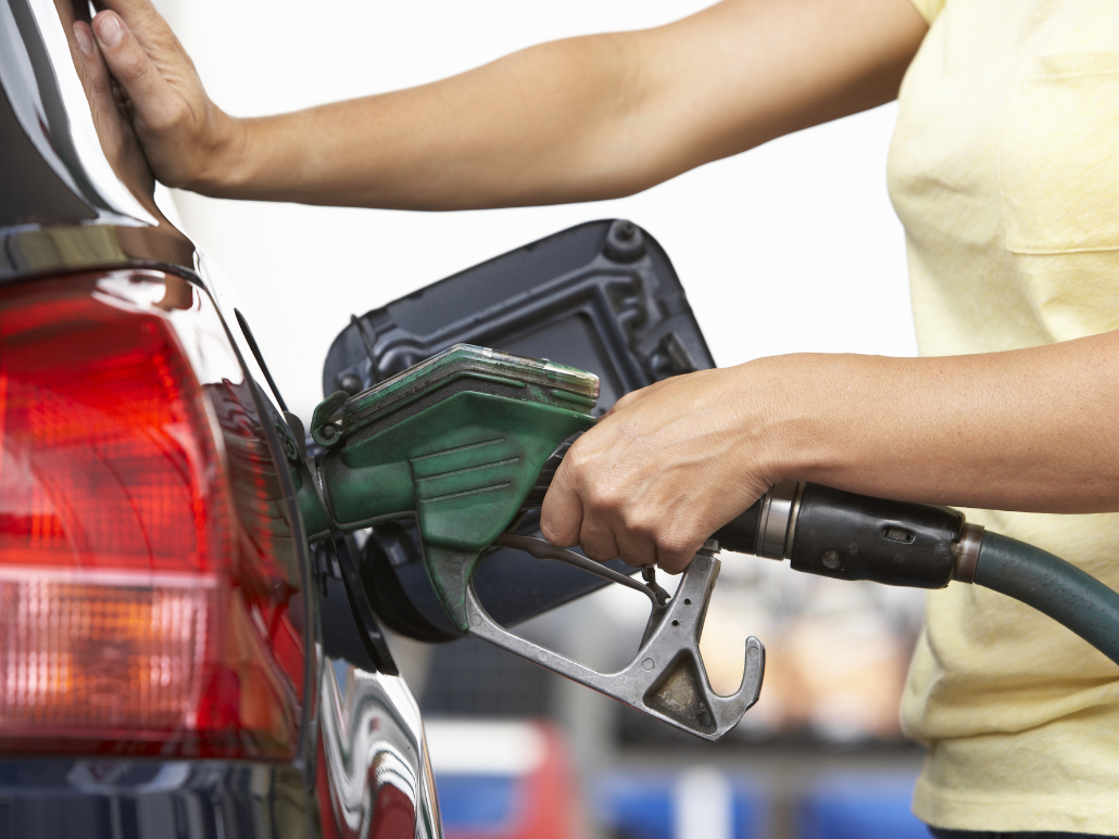 Close-up of a person refueling a car, holding a green fuel nozzle and pressing the car with the other hand.