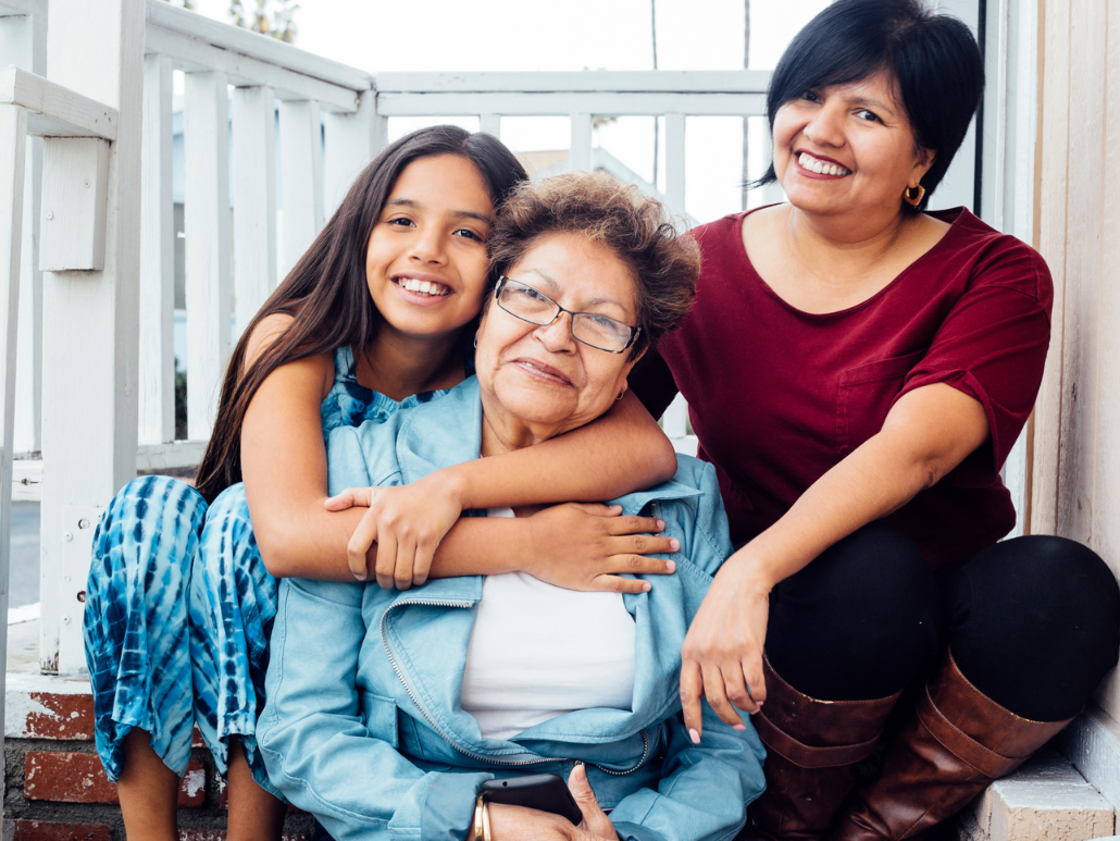 Three generations of women sitting together on a porch, smiling at the camera.