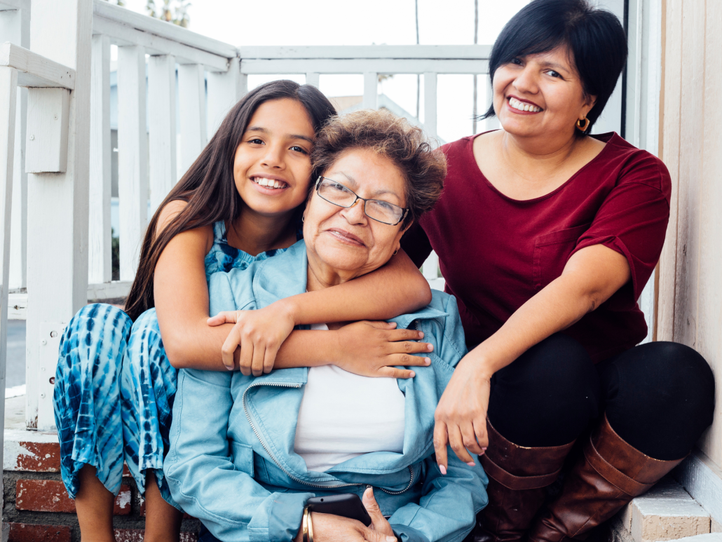 Three generations of women sitting together on a porch, smiling at the camera.