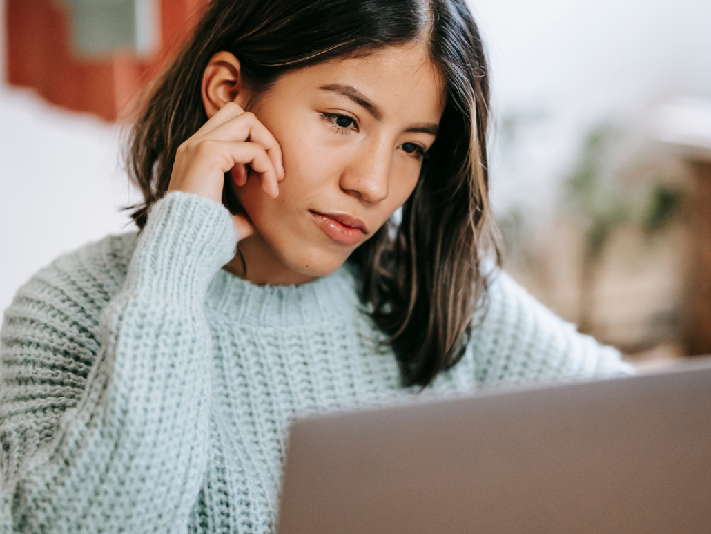 Mujer con suéter azul claro mirando pensativamente la pantalla de una computadora.