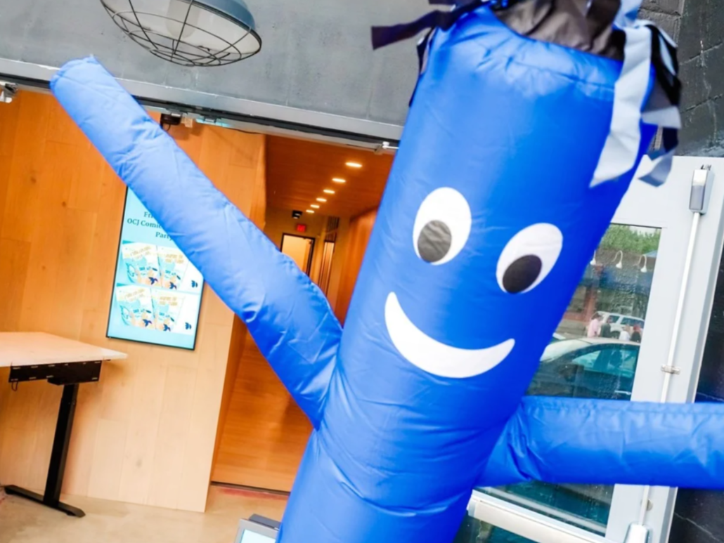 Blue inflatable floppy tube guy with a smiley face at an event entrance.