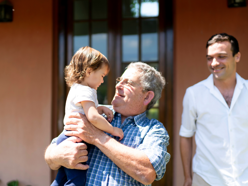 An older man holding a young child while another man stands nearby, all smiling.