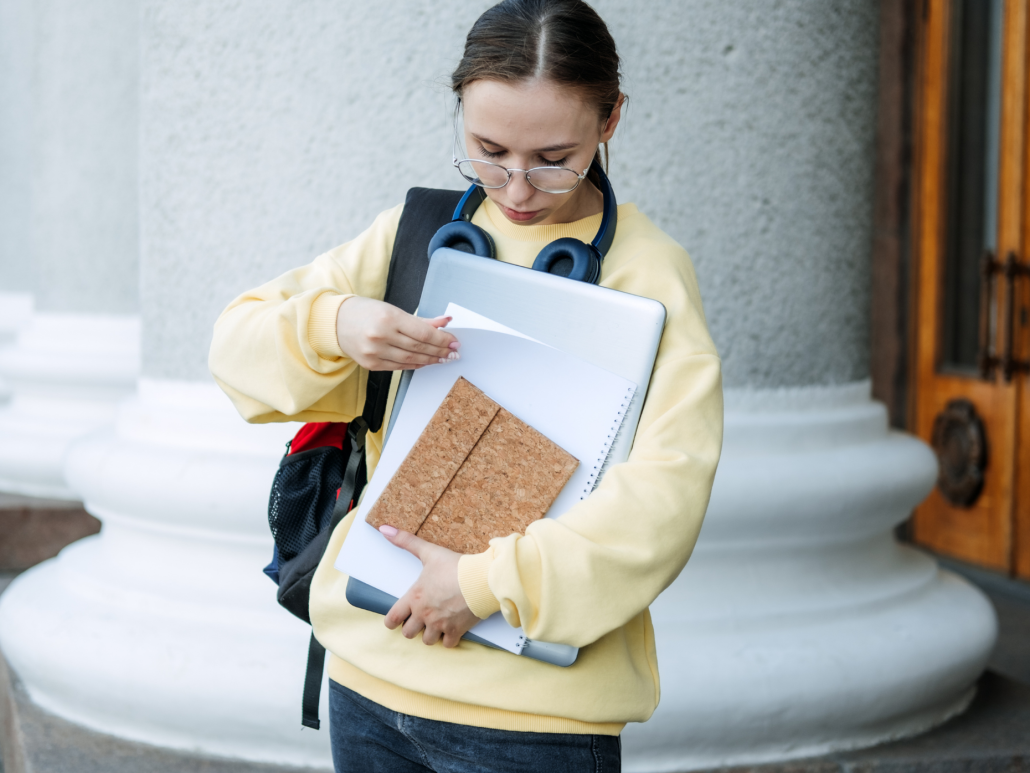 Student looking at a notebook outside a building with columns.