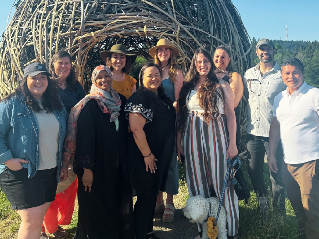 Group photo of ten OCJ team members standing and smiling in front of a large outdoor woven structure.