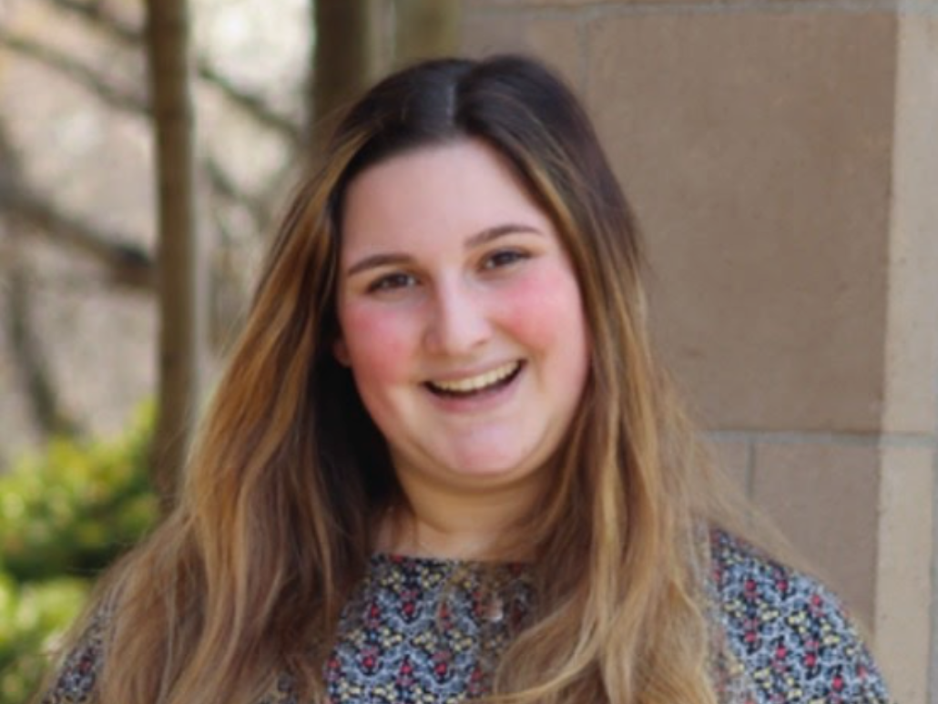 Headshot of Kat smiling outdoors near a brick column.