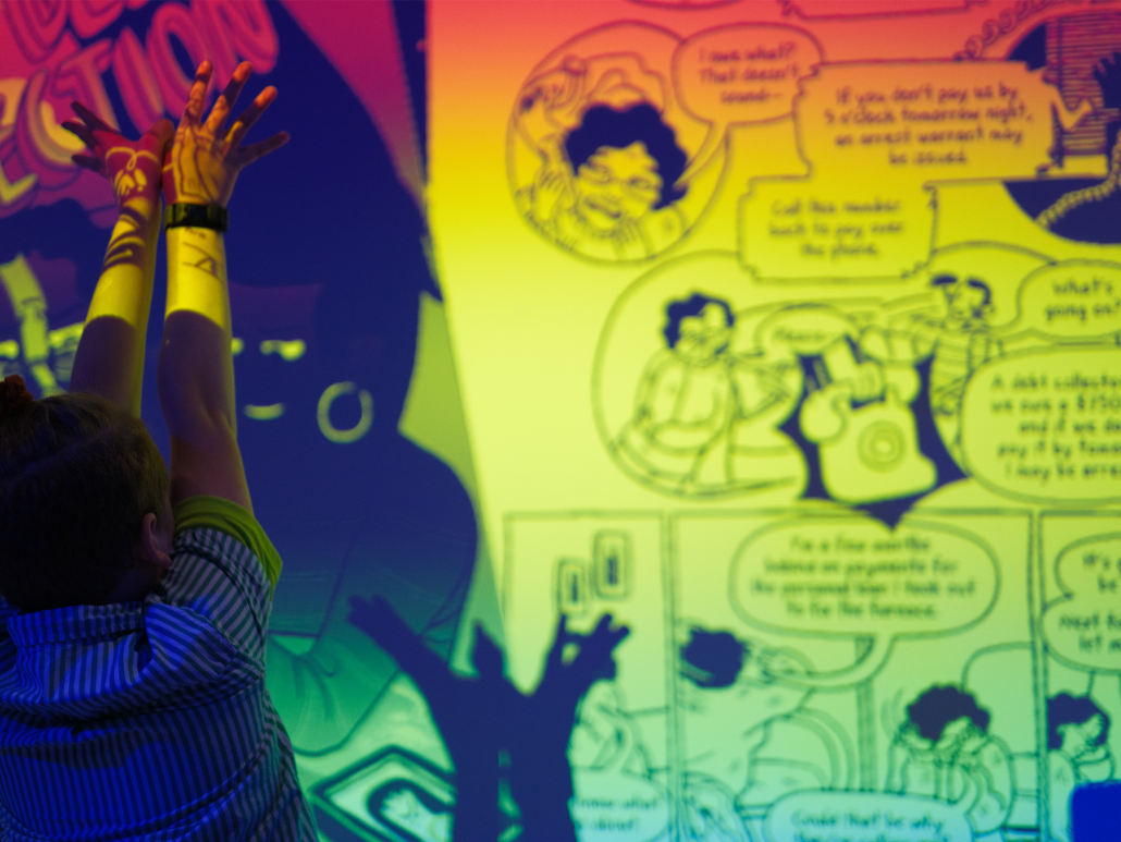 A silhouetted person raising their hands in front of the projector displaying a page of the Dealing with Debt Collection comic book.