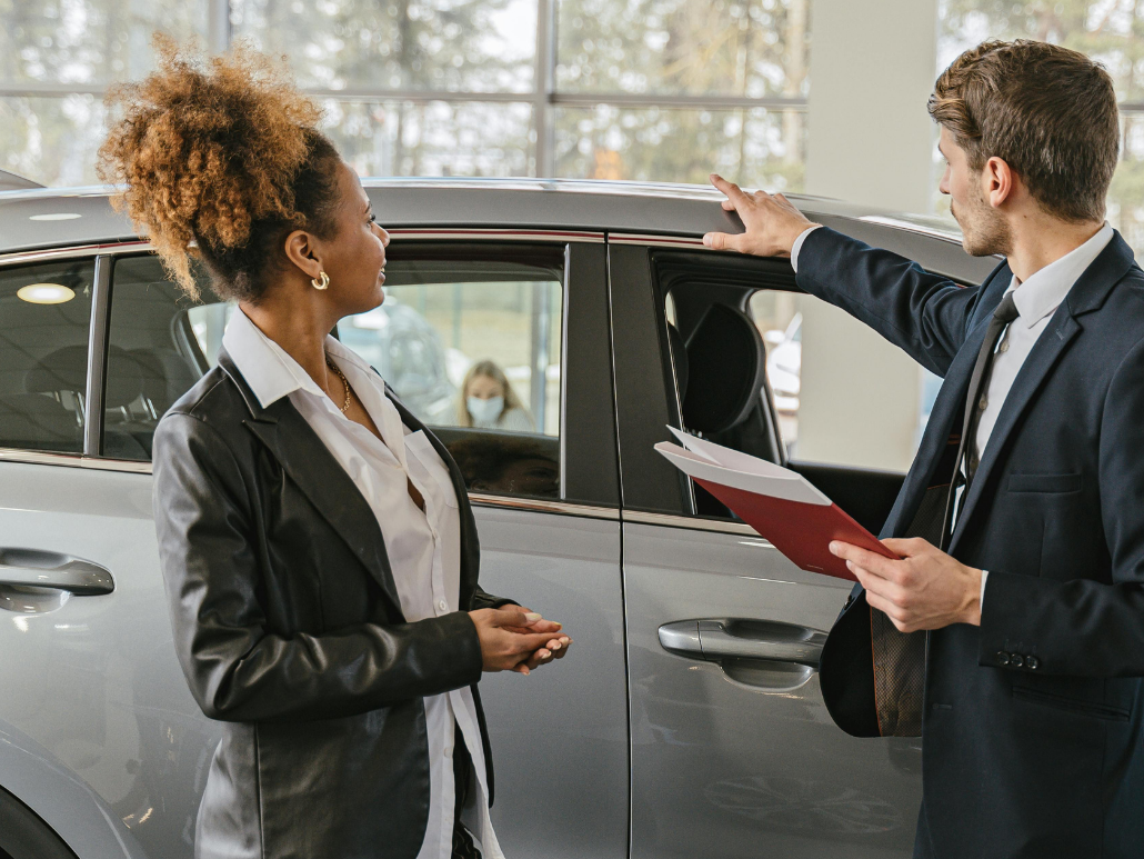 Two people are standing in front of a car in a showroom.