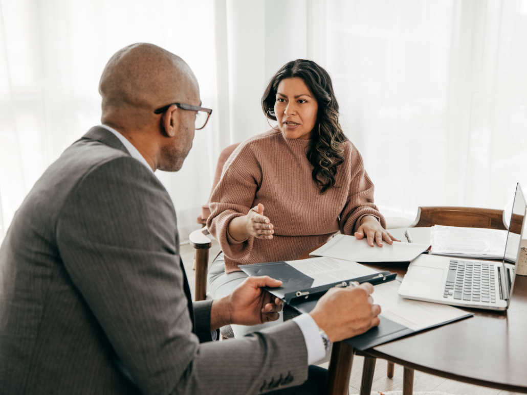 Two people sitting at a table with documents on it having a conversation.