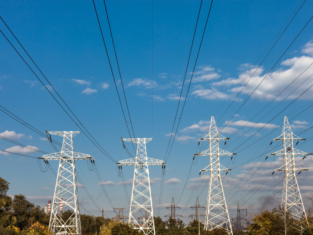 Four white transmission towers standing in a field against a blue sky.