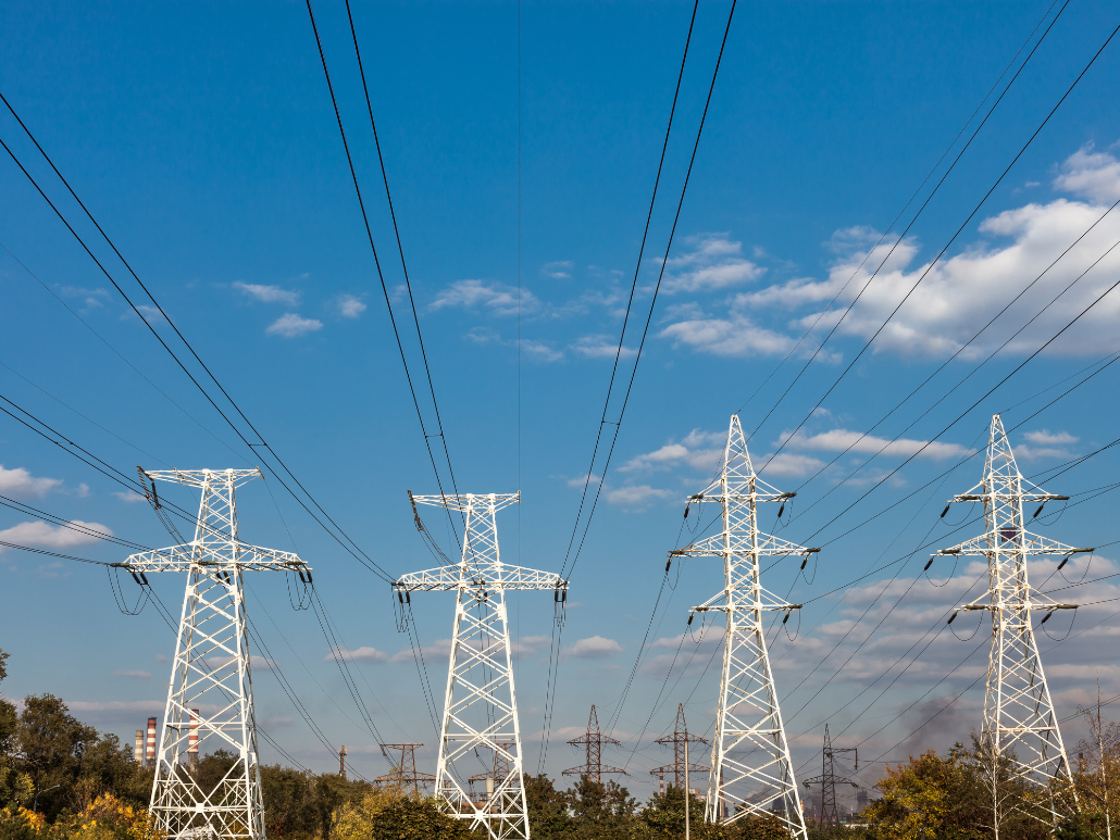 A photo of four power lines standing in a green field against a blue sky.