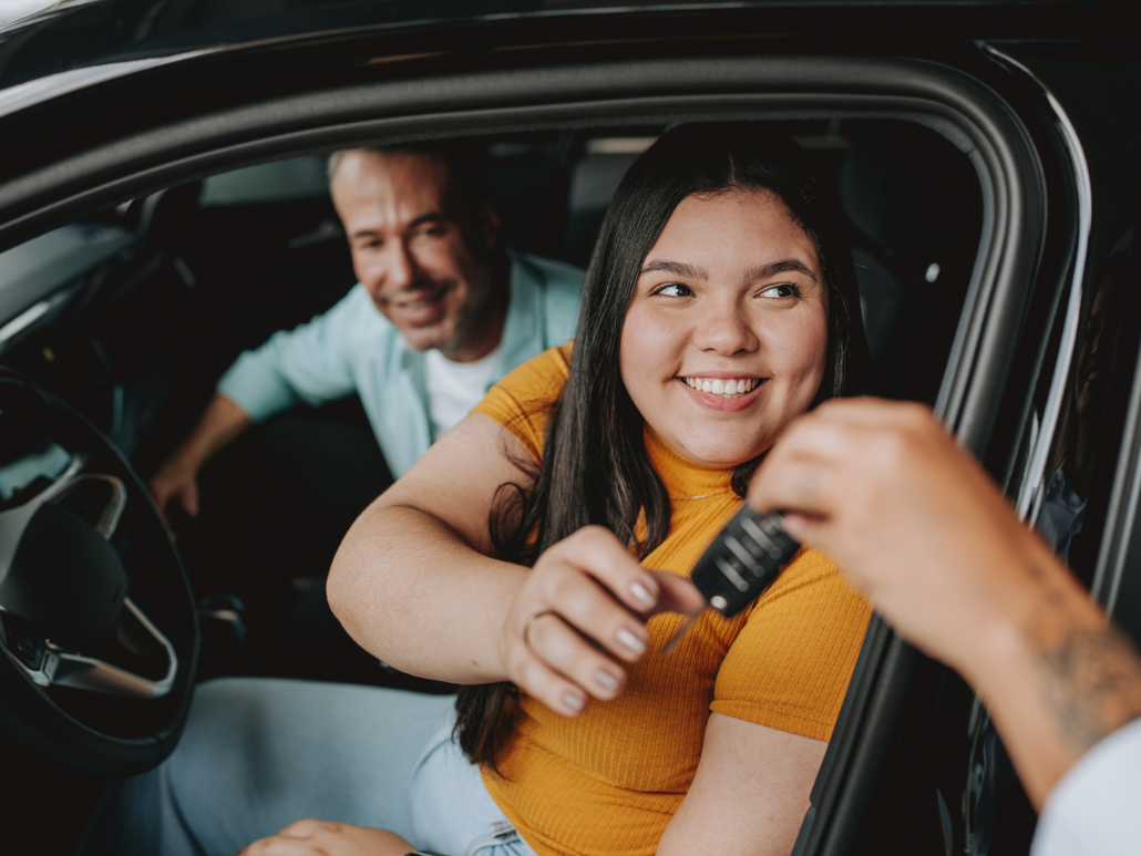 A woman smiling grabbing car keys while sitting in the driver's seat.