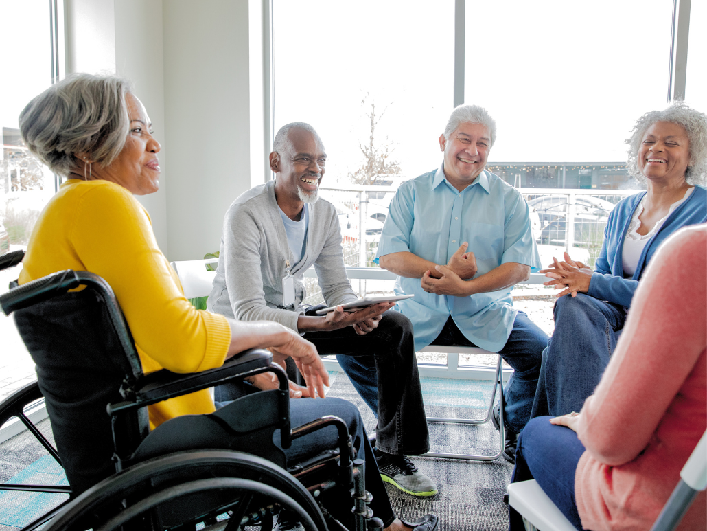 A group of older adults sitting on chairs in a circle. One woman is in a wheelchair.
