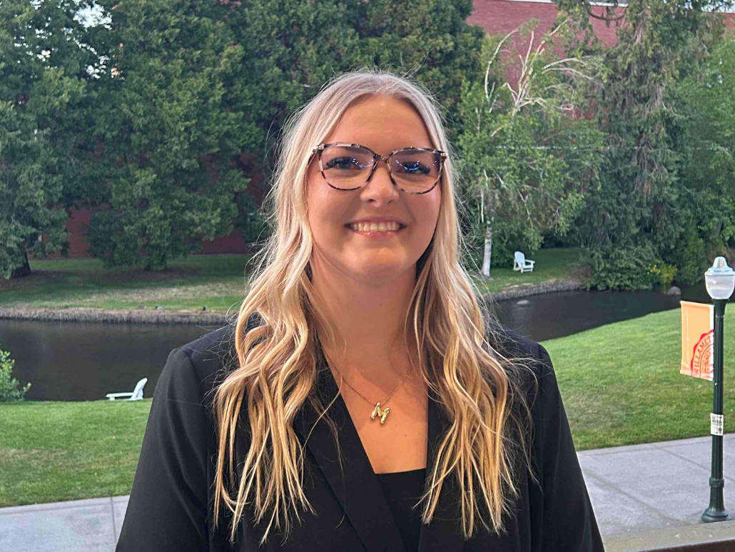 身着西装、打着领带的 Nik 在户外微笑的肖像，背景为绿色植物。