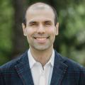 Man smiling at the camera in a suit with a out of focus natural background