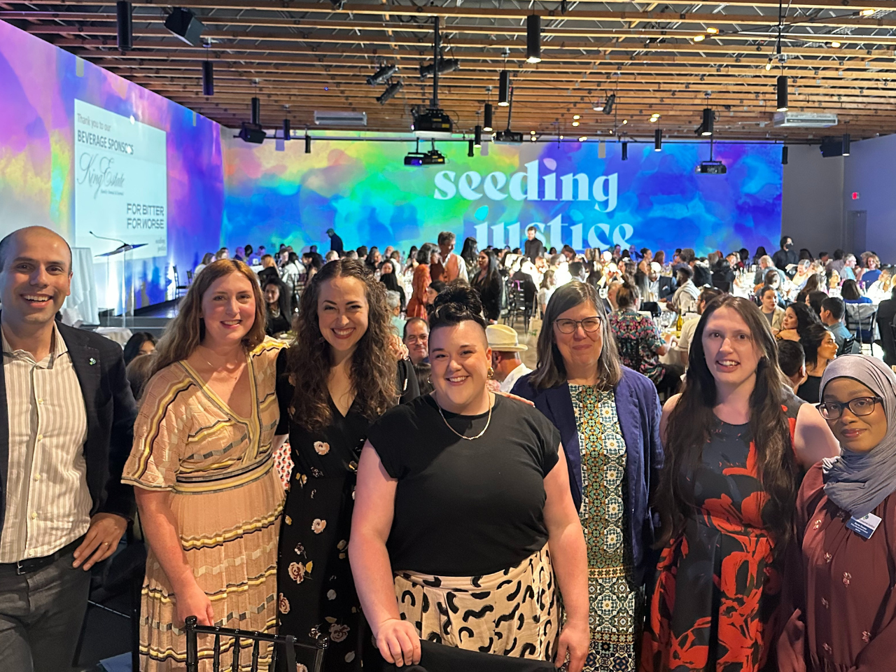 Group photo of seven OCJ team members standing together at Justice Within Reach, an event put on by community partner, Seeding Justice. The words "seeding justice" projected on the wall in the background.