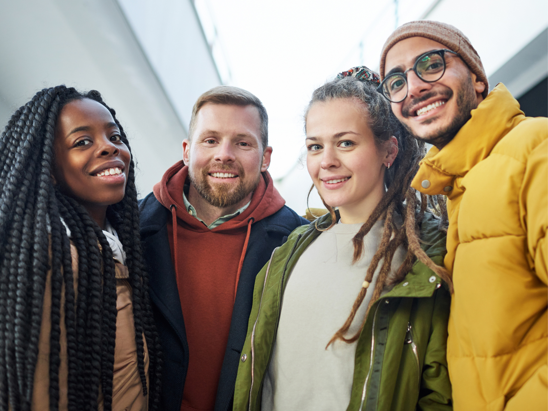 A group of four diverse young adults smiling together, wearing casual and winter clothing.