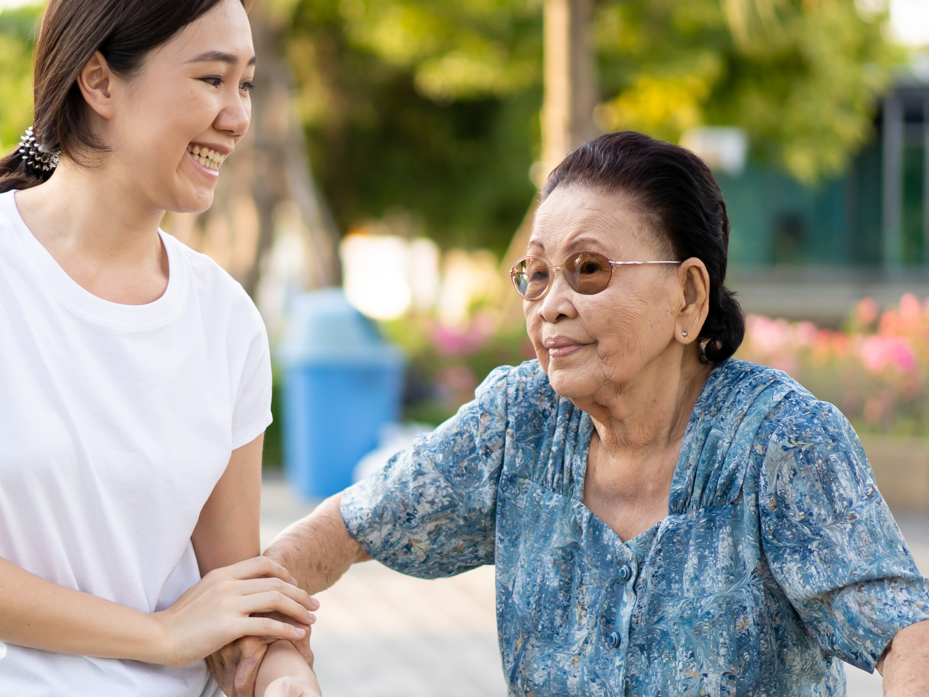 A young woman in a white shirt assisting an older woman with a walker in a park setting.