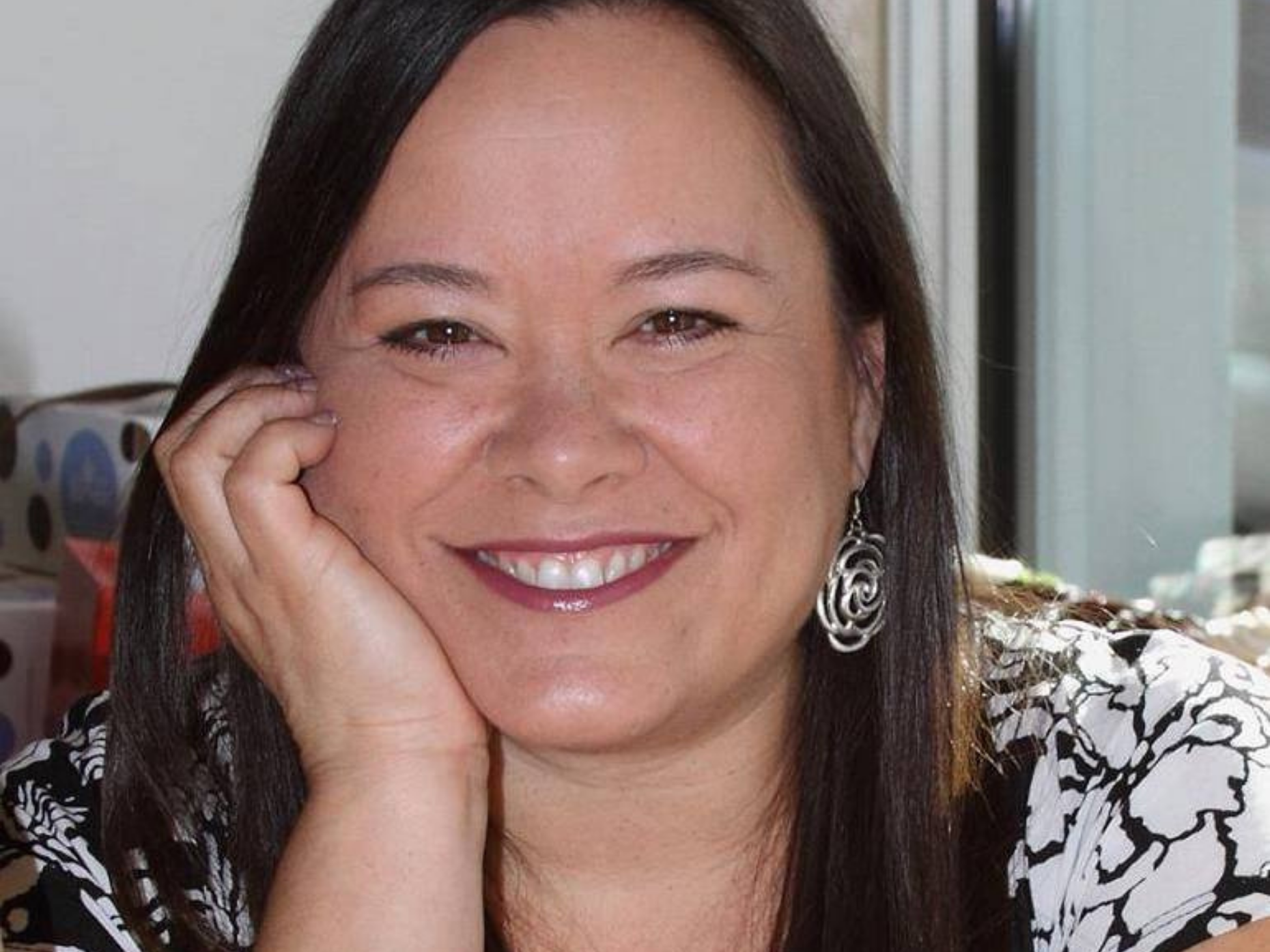 Portrait of associate director, Lisa Watson, with long dark hair, resting her head on her hand.