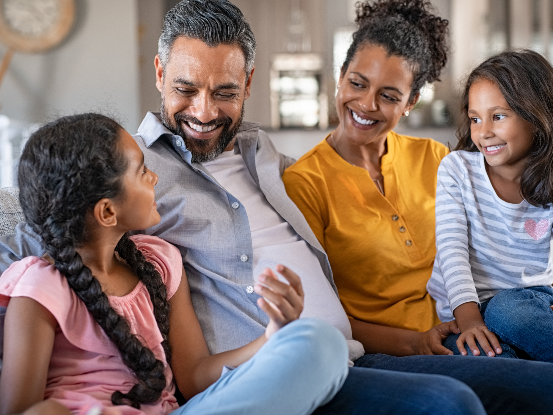 Happy family of four sitting on a couch and smiling at each other.