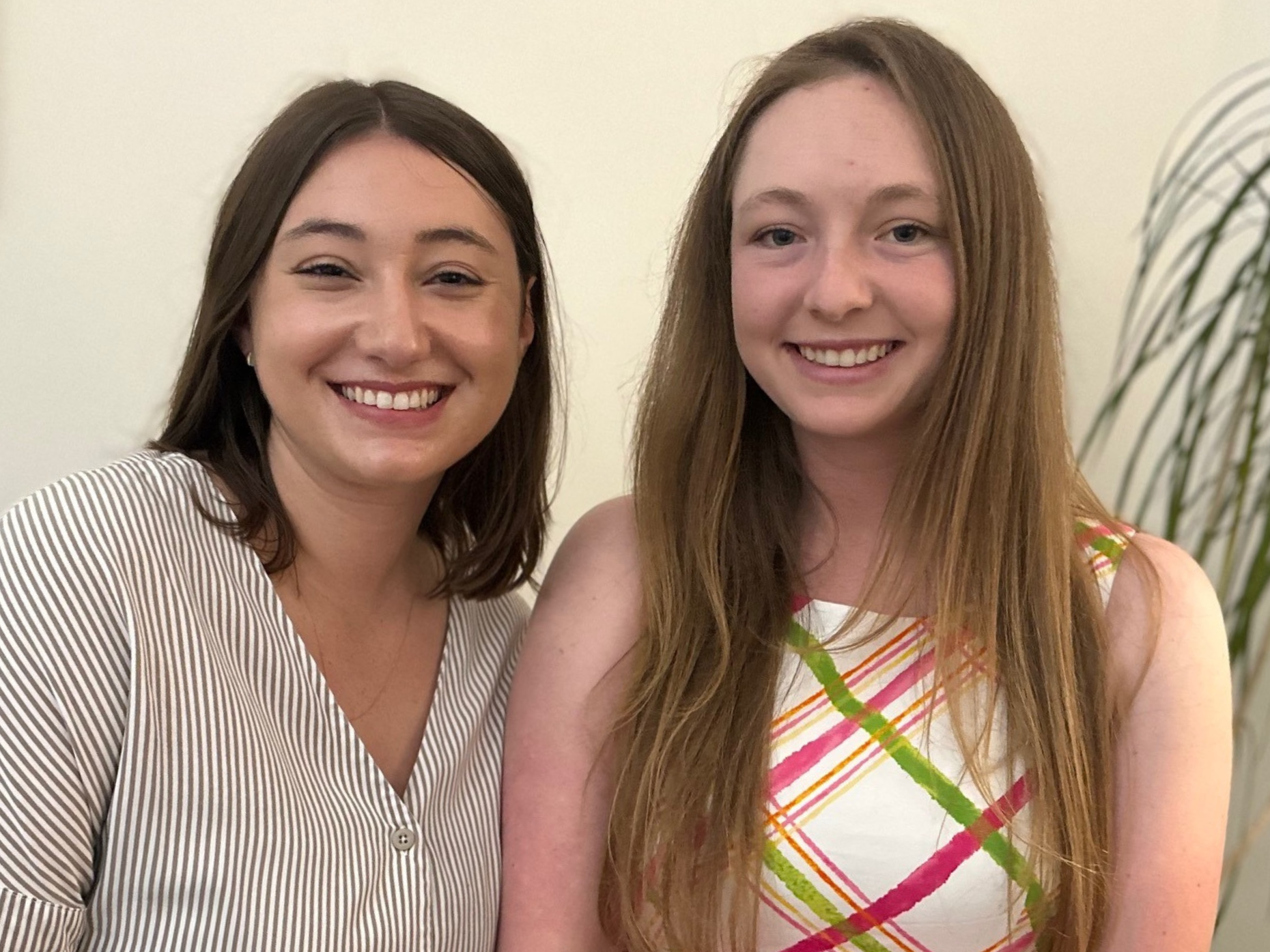 Summer interns smiling at the camera, Megan is wearing a striped shirt and Samantha has on a colorful patterned dress.