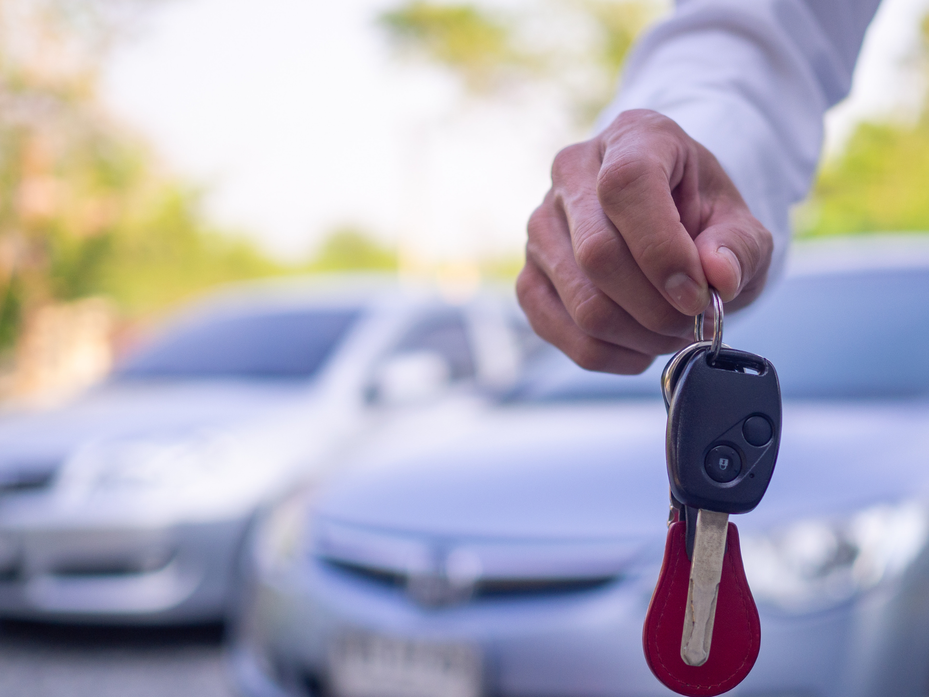 Hand holding car keys with cars in the background.