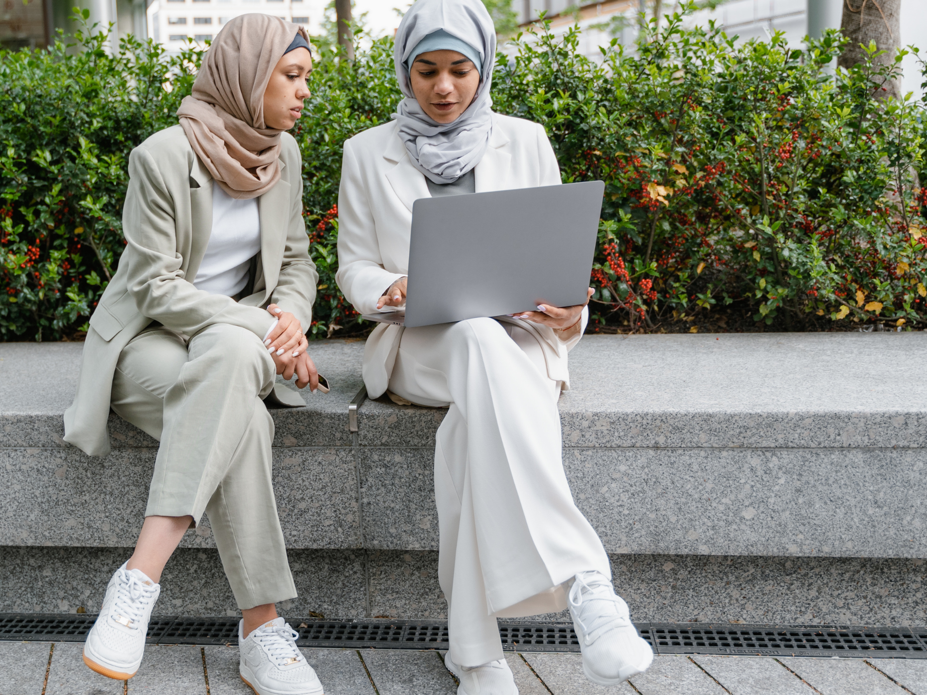 Two women in hijabs working on a laptop outdoors.