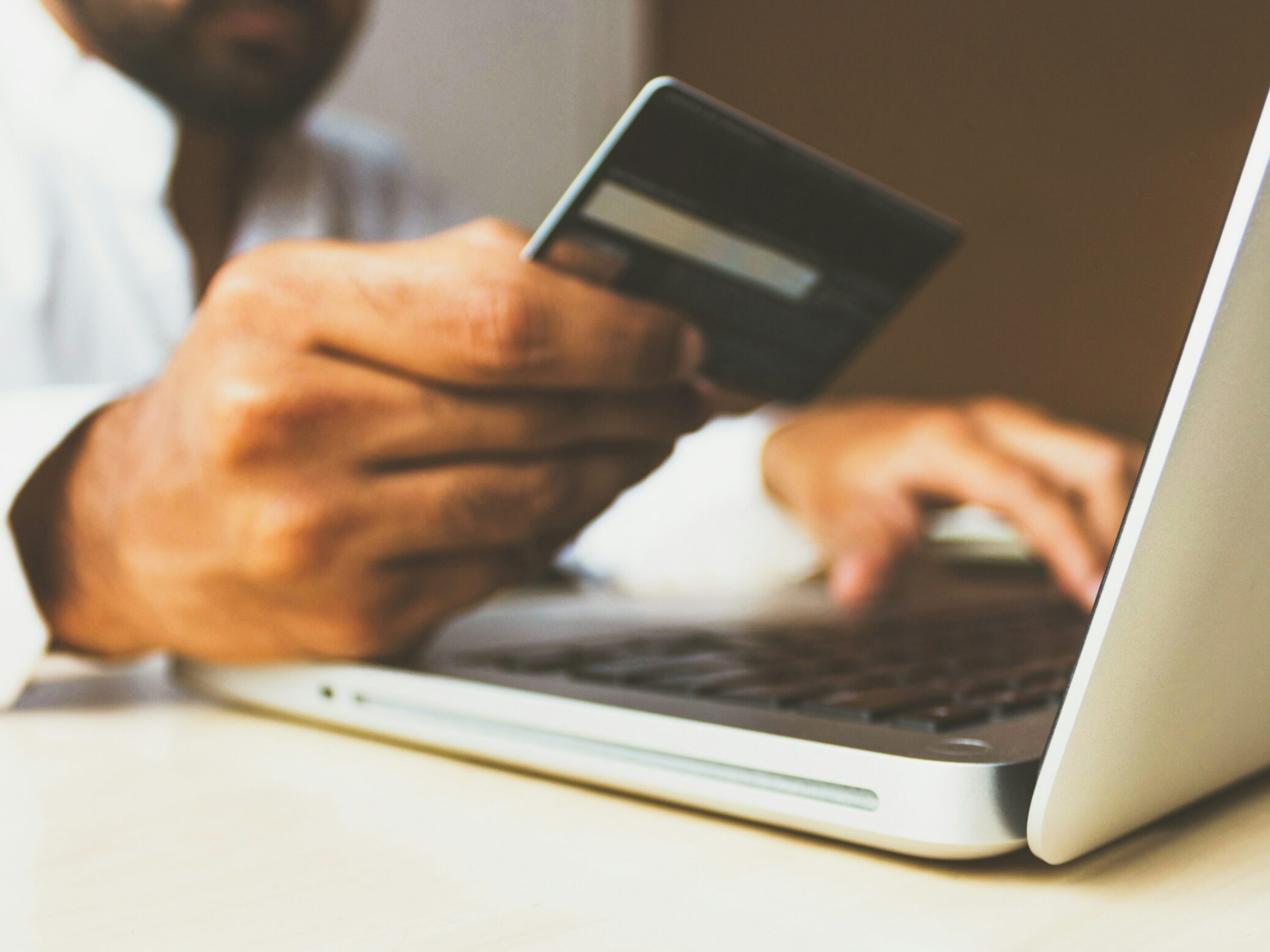 Close-up of a person holding a credit card and typing on a laptop.