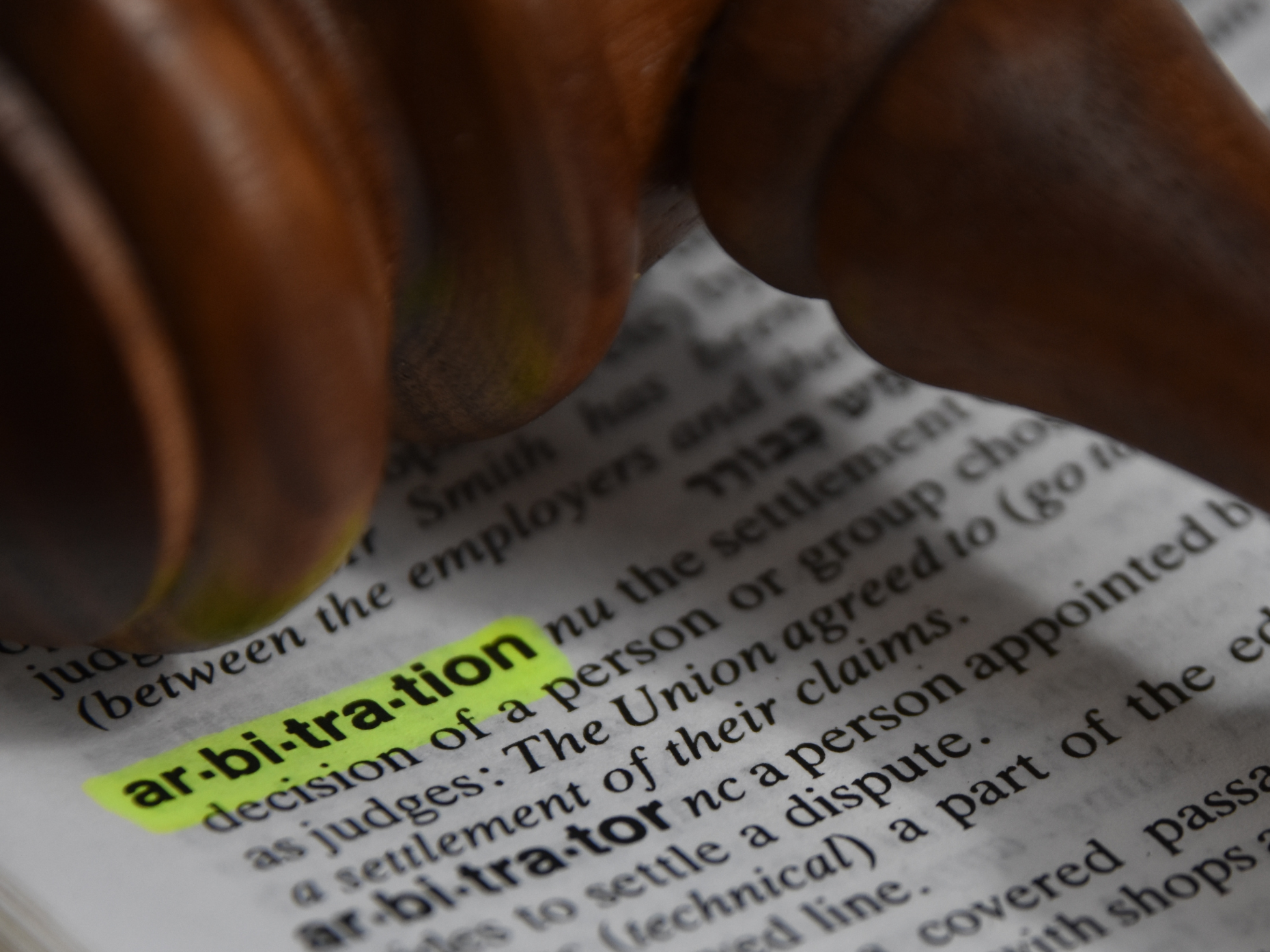 Close-up of a gavel resting on a dictionary with the word "arbitration" highlighted.