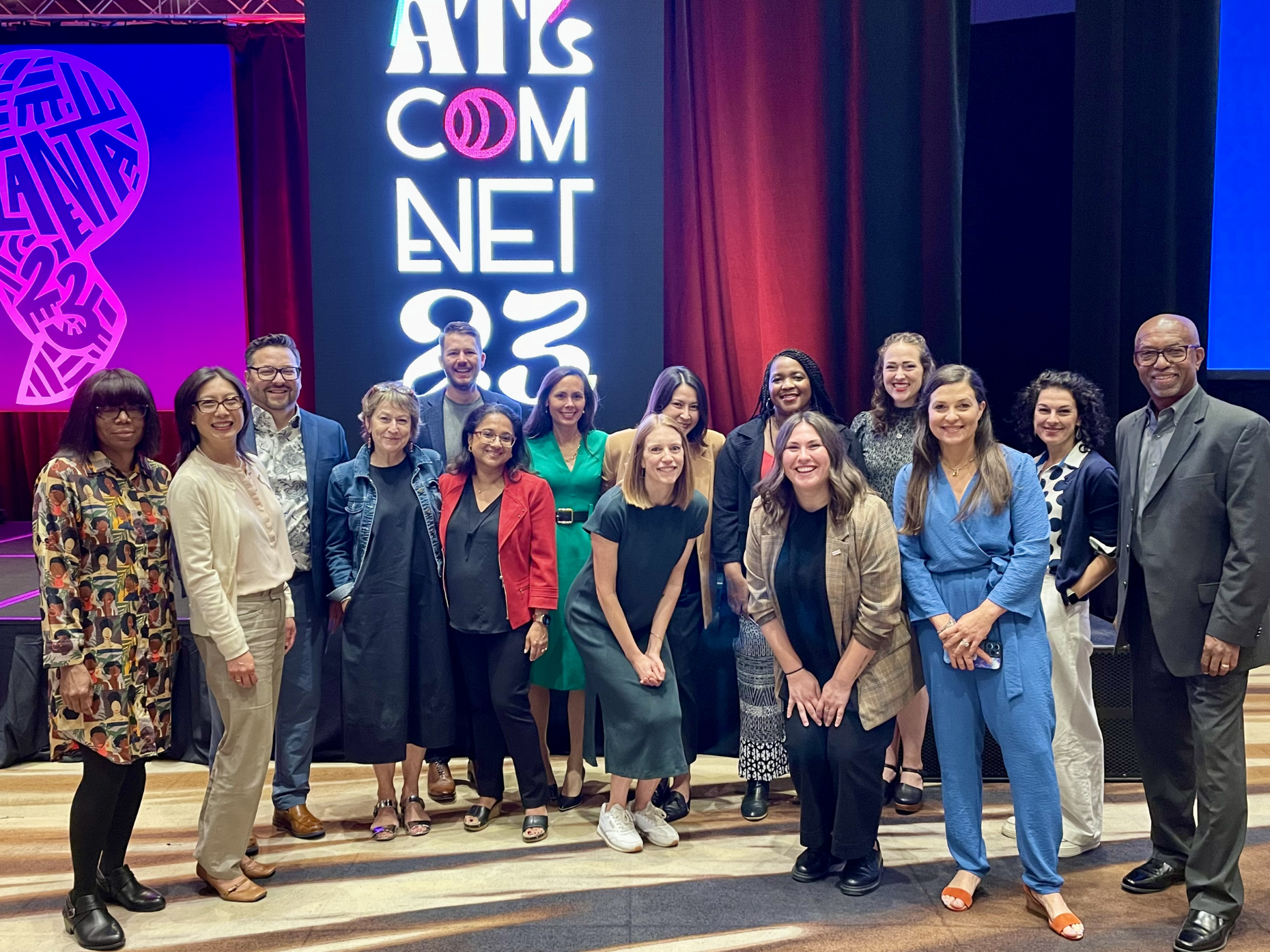 A group of communications professionals stands in front of signage for ComNet23 in Atlanta.