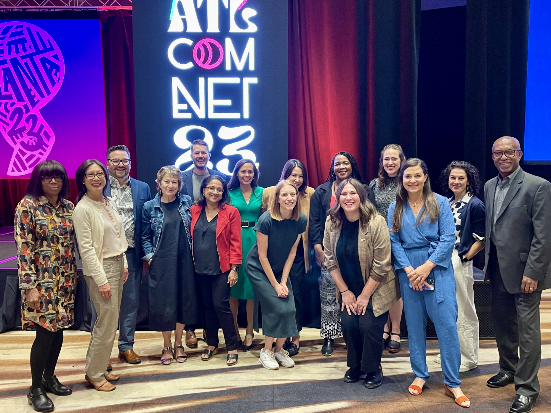 A group of communications professionals stands in front of signage for ComNet23 in Atlanta. 