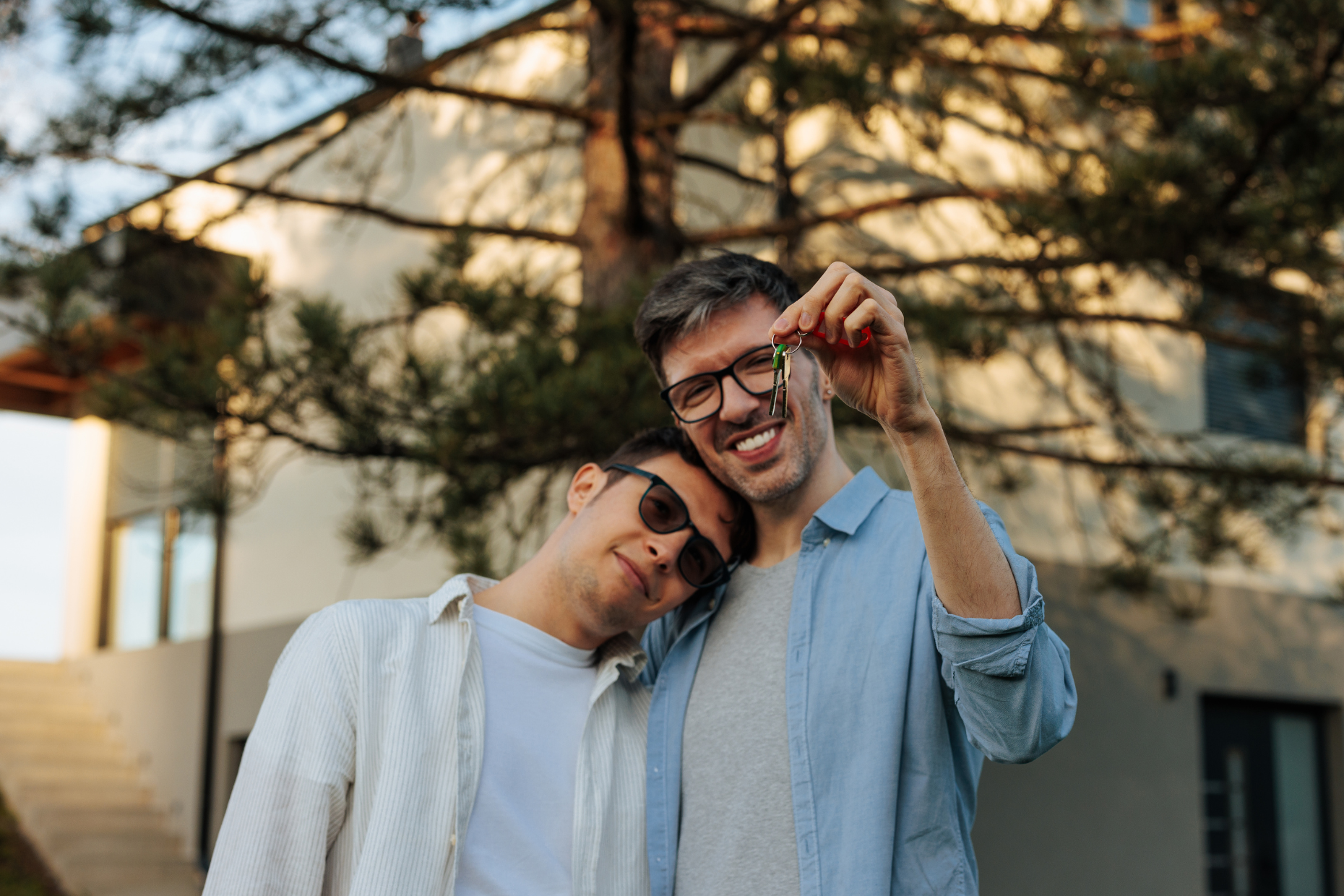 A couple standing in front of a new house holding keys.