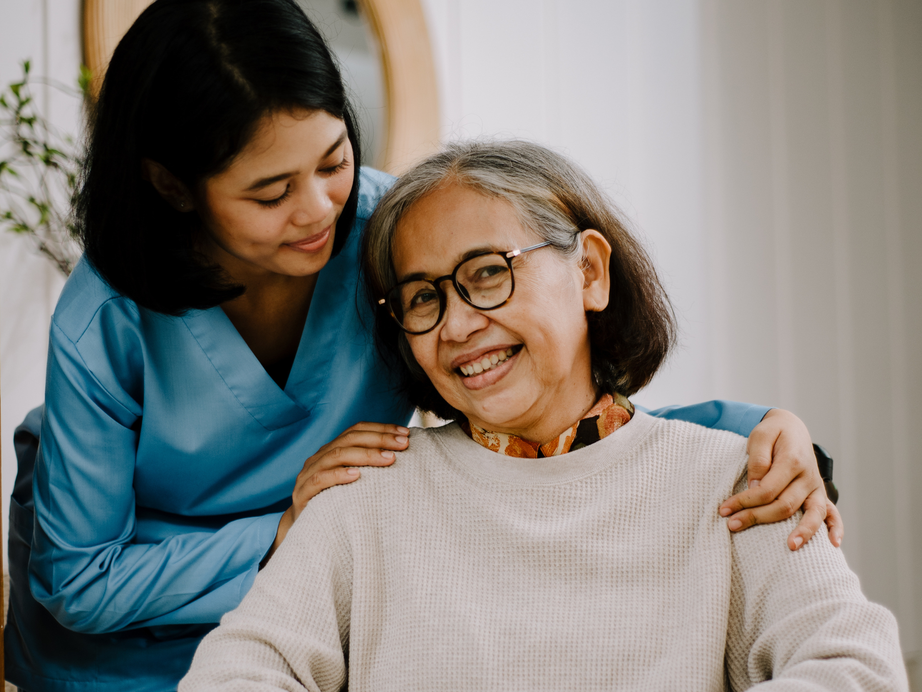 A woman putting her hands on the shoulders of an older woman sitting down.