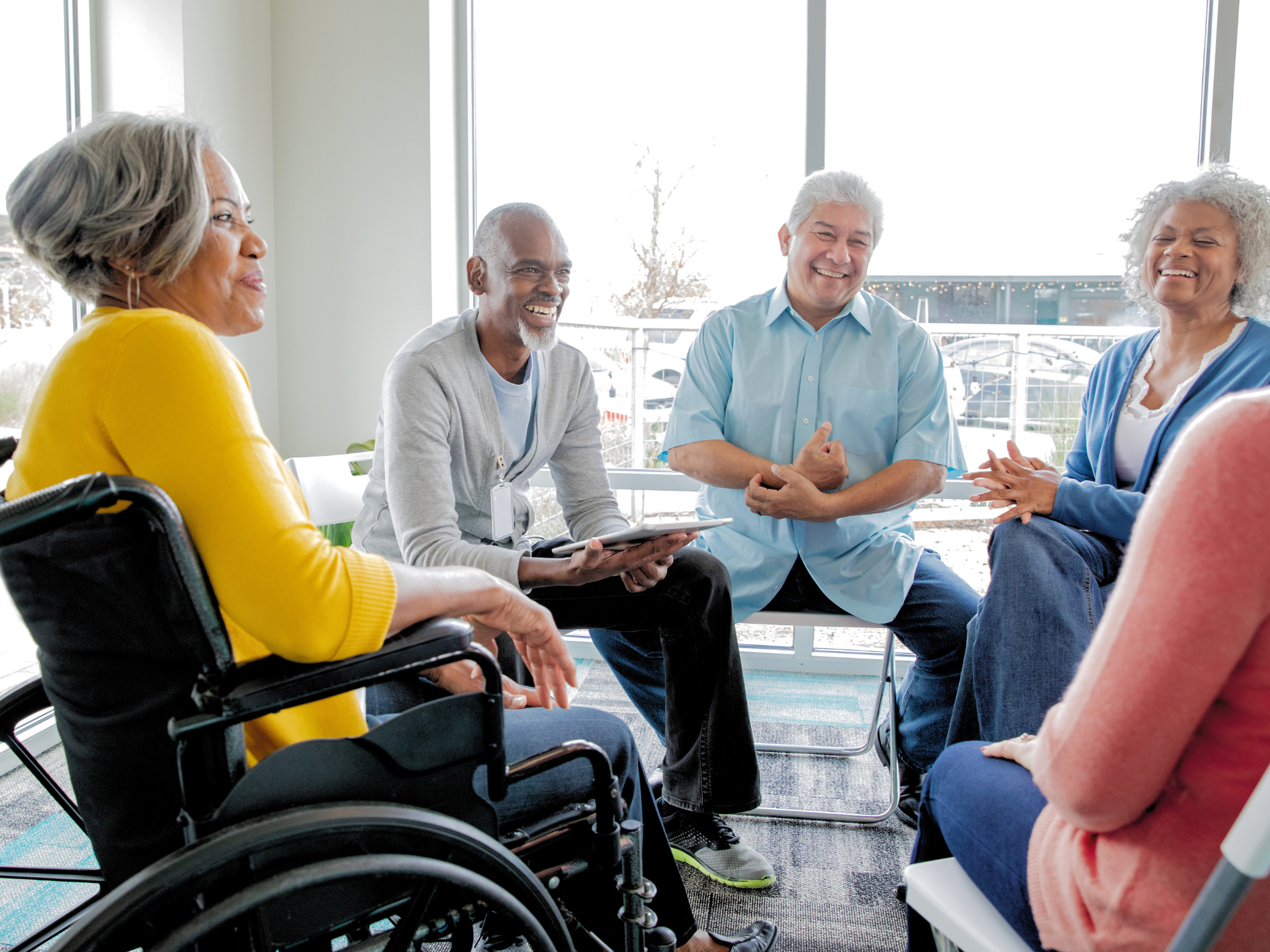 A group of older adults sitting on chairs in a circle. One woman is in a wheelchair.