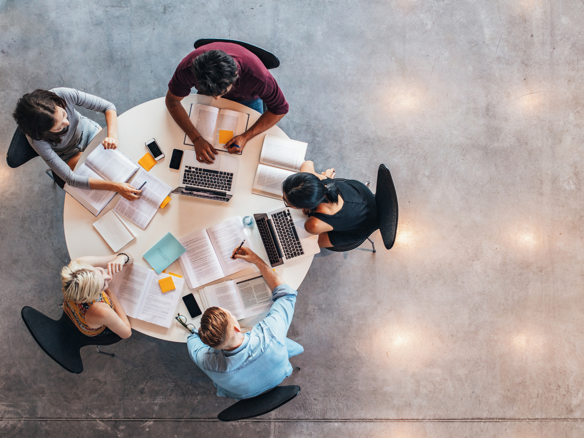A birds eye shot of a group of people sitting around a table talking and working on computers.