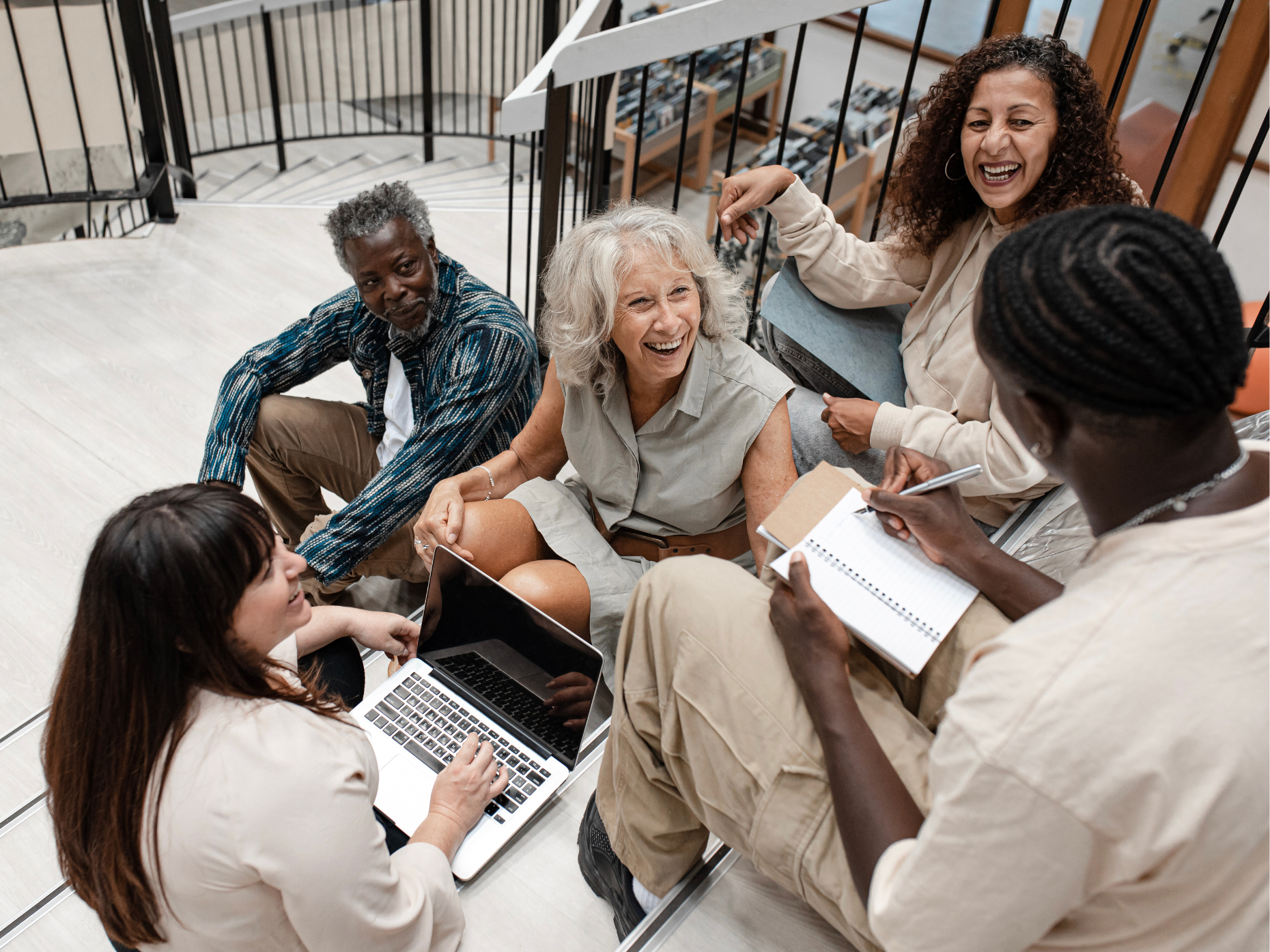 A group of people of varying ages and skin tones sitting on library stairs talking and laughing.