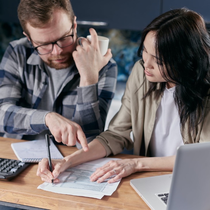 A man and woman sitting at a table with a laptop, calculator, and documents, discussing financial matters.