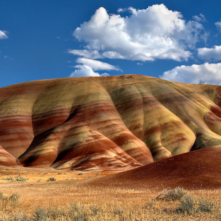 Landscape of colorful, stratified hills under a partly cloudy sky.