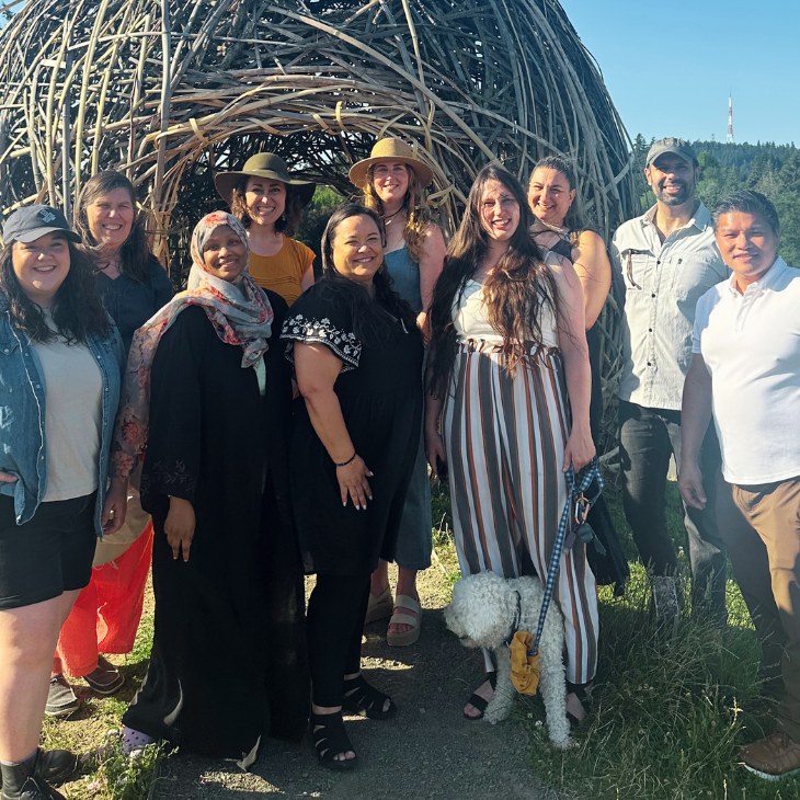 Group photo of ten OCJ team members standing and smiling in front of a large outdoor woven structure.