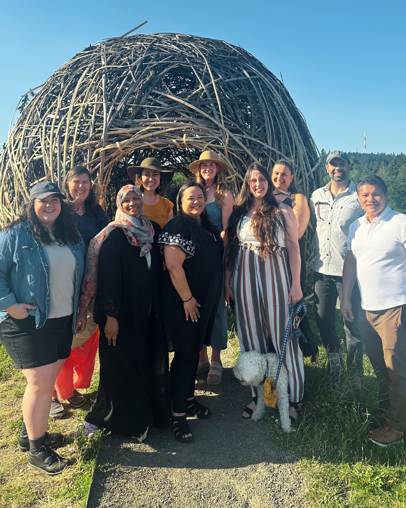 Group photo of ten OCJ team members standing and smiling in front of a large outdoor woven structure.