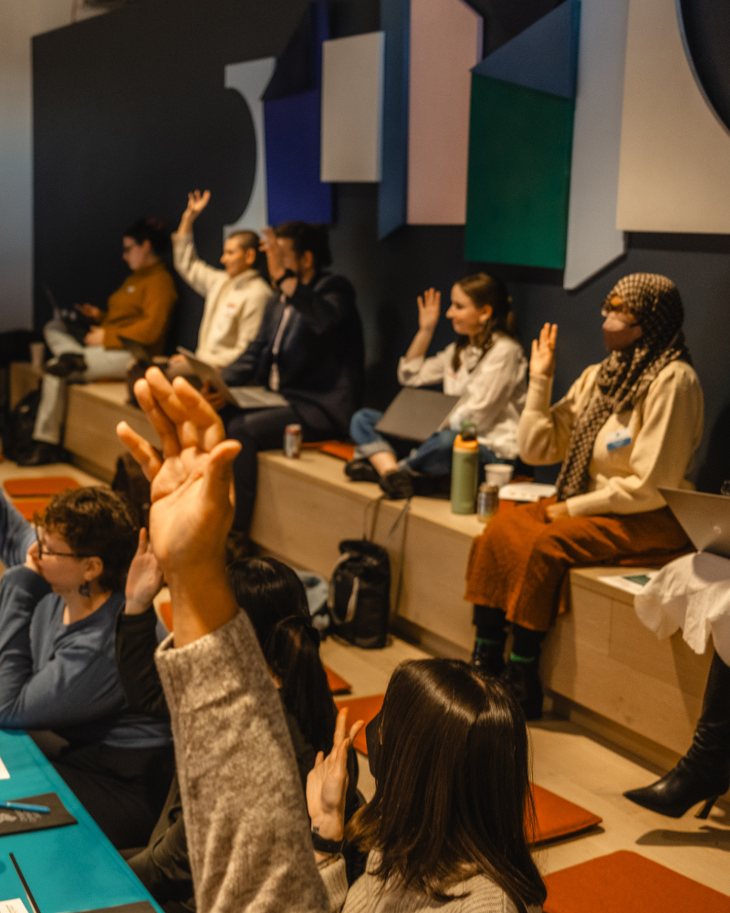 A group of people sitting at an event raising their hands.